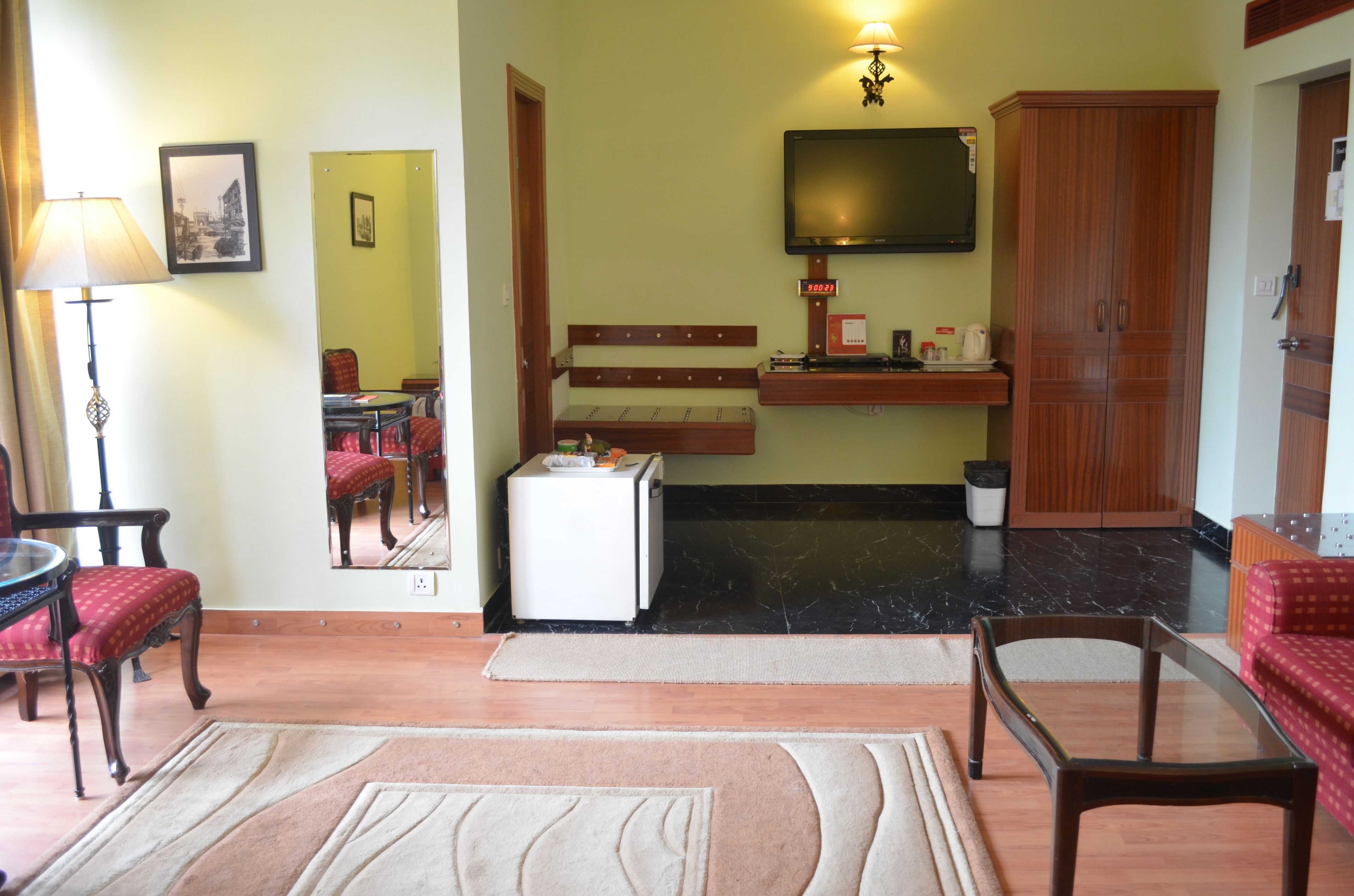 A living room with a television, a small refrigerator, a wooden cabinet, and a red sofa.