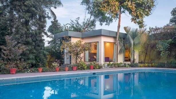 A modern house with a pool, surrounded by lush greenery and trees. - The Radha Ashok (Mathura)