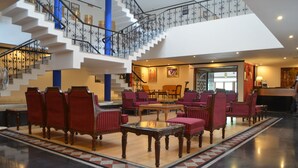 A spacious lobby with a grand staircase, red upholstered chairs, and a polished floor. - The Radha Ashok (Mathura)