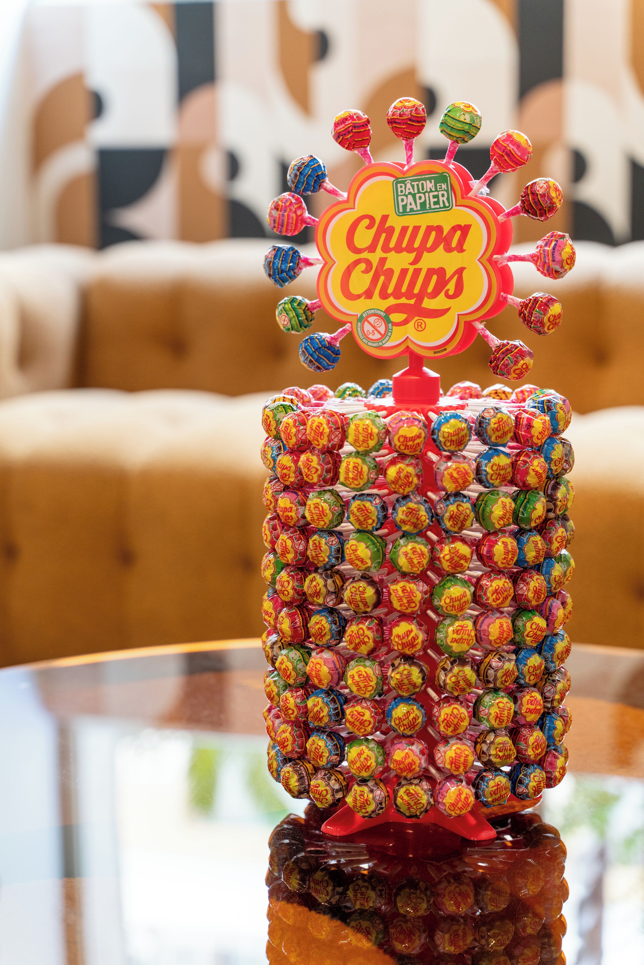 Un arbre decoratiu fet amb caramels Chupa Chups sobre una taula de vidre.