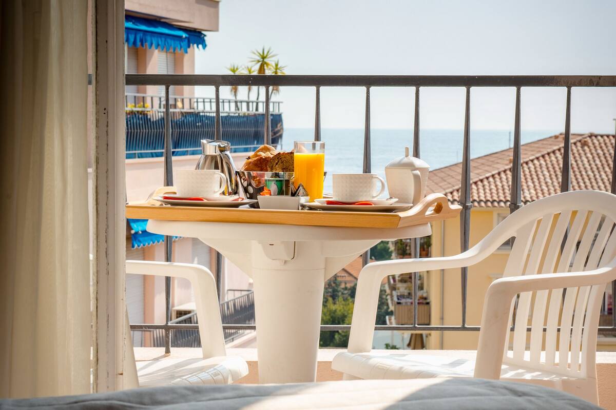 A balcony with a table set for breakfast, including a coffee pot, cups, and a glass of orange juice.