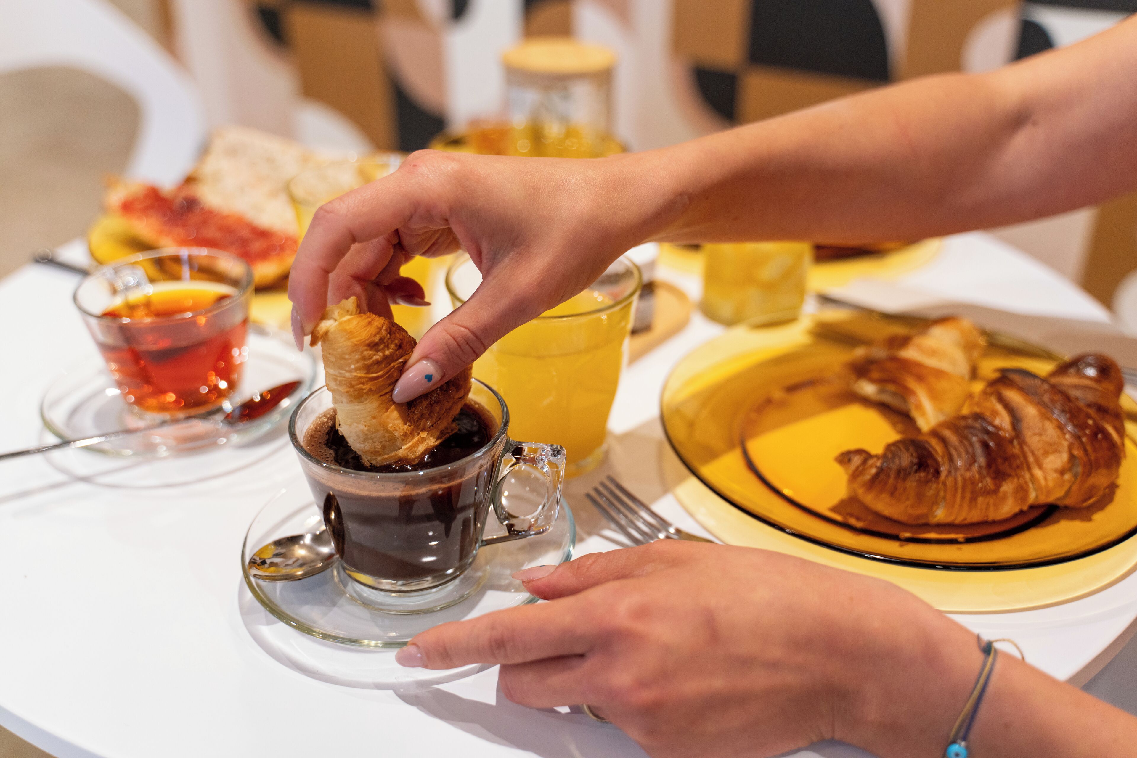 A breakfast setting with croissants, orange juice, and a cup of coffee on a table.