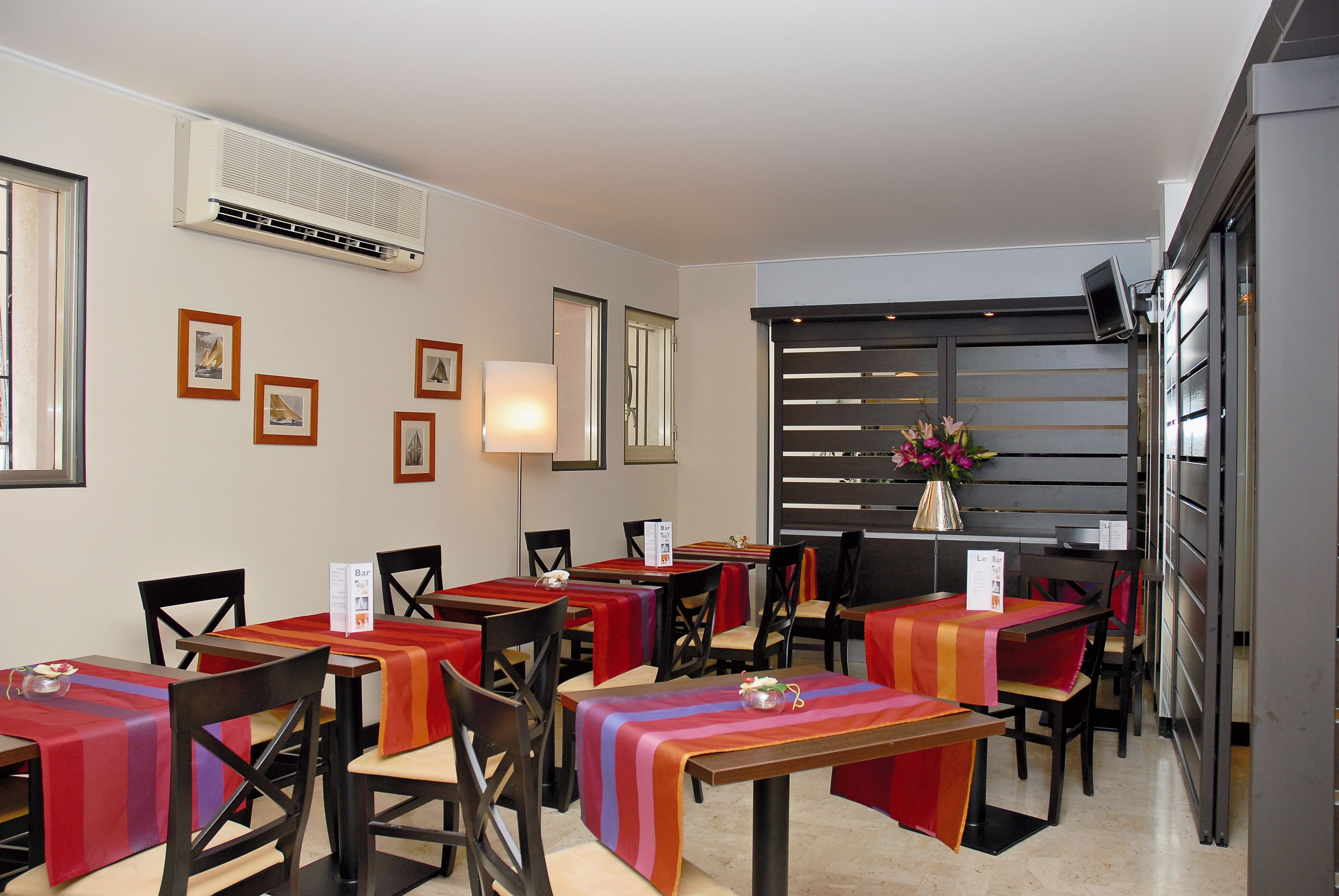Un comedor con mesas cubiertas con manteles coloridos, sillas y un aire acondicionado instalado en la pared.