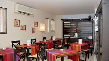 Un comedor con mesas cubiertas con manteles coloridos, sillas y un aire acondicionado instalado en la pared.