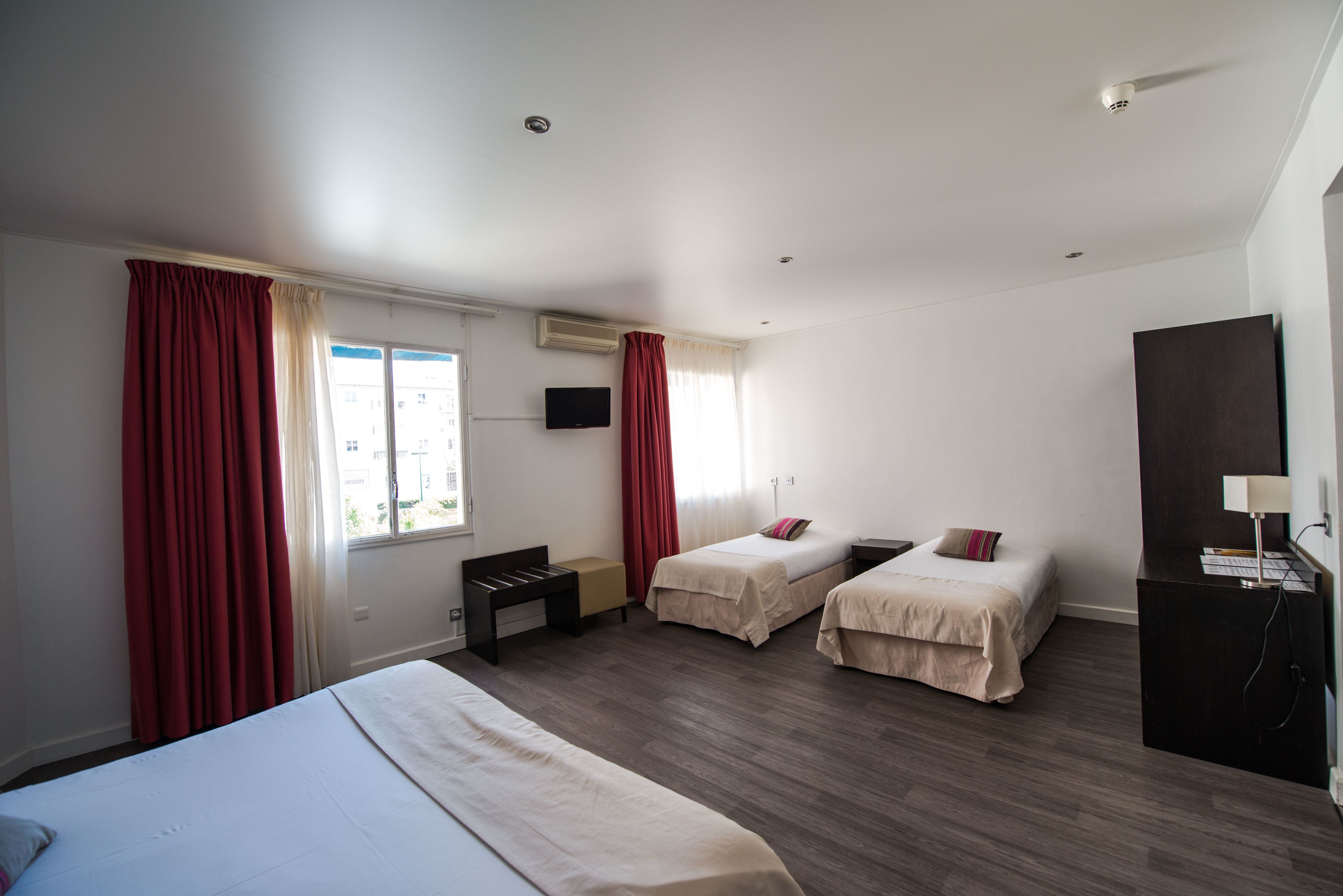 Habitación de hotel con dos camas individuales, un escritorio, una silla, un televisor y un armario.