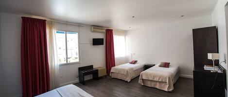 Habitación de hotel con dos camas individuales, un escritorio, una silla, un televisor y un armario.