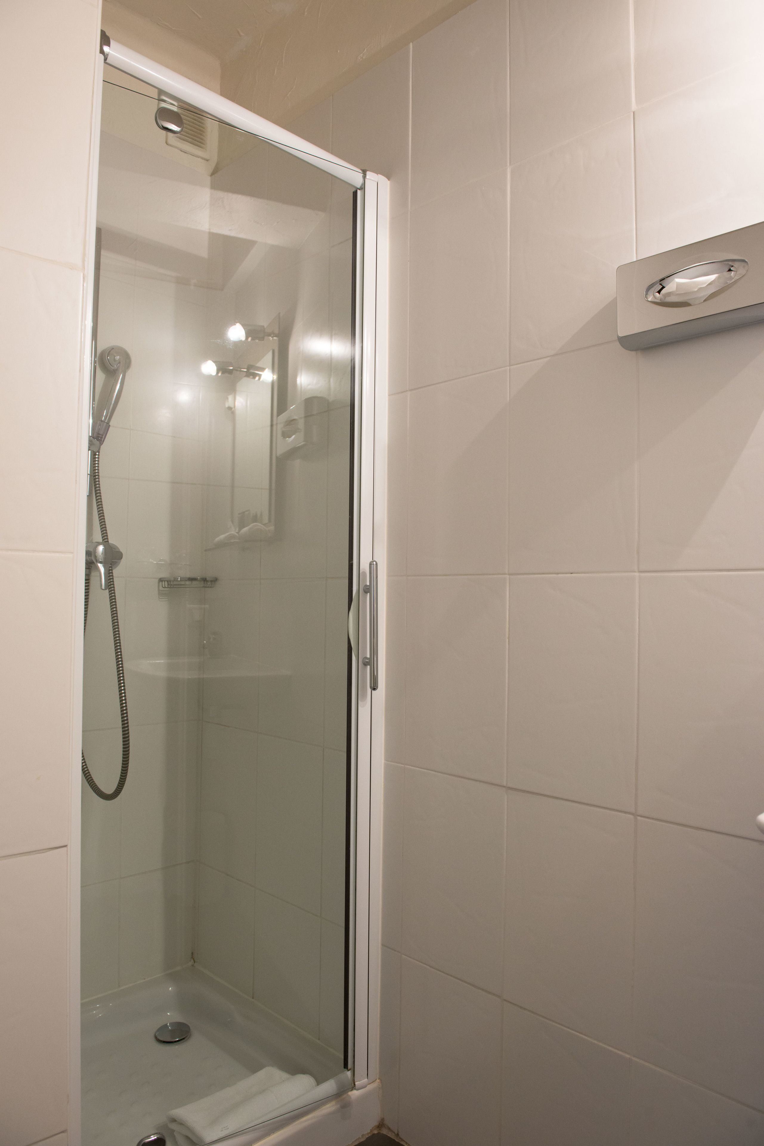 A glass-enclosed shower with a handheld showerhead and a wall-mounted control panel.