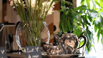 Un florero de cristal transparente con flores blancas, una tetera de plata y una taza a juego sobre una bandeja.