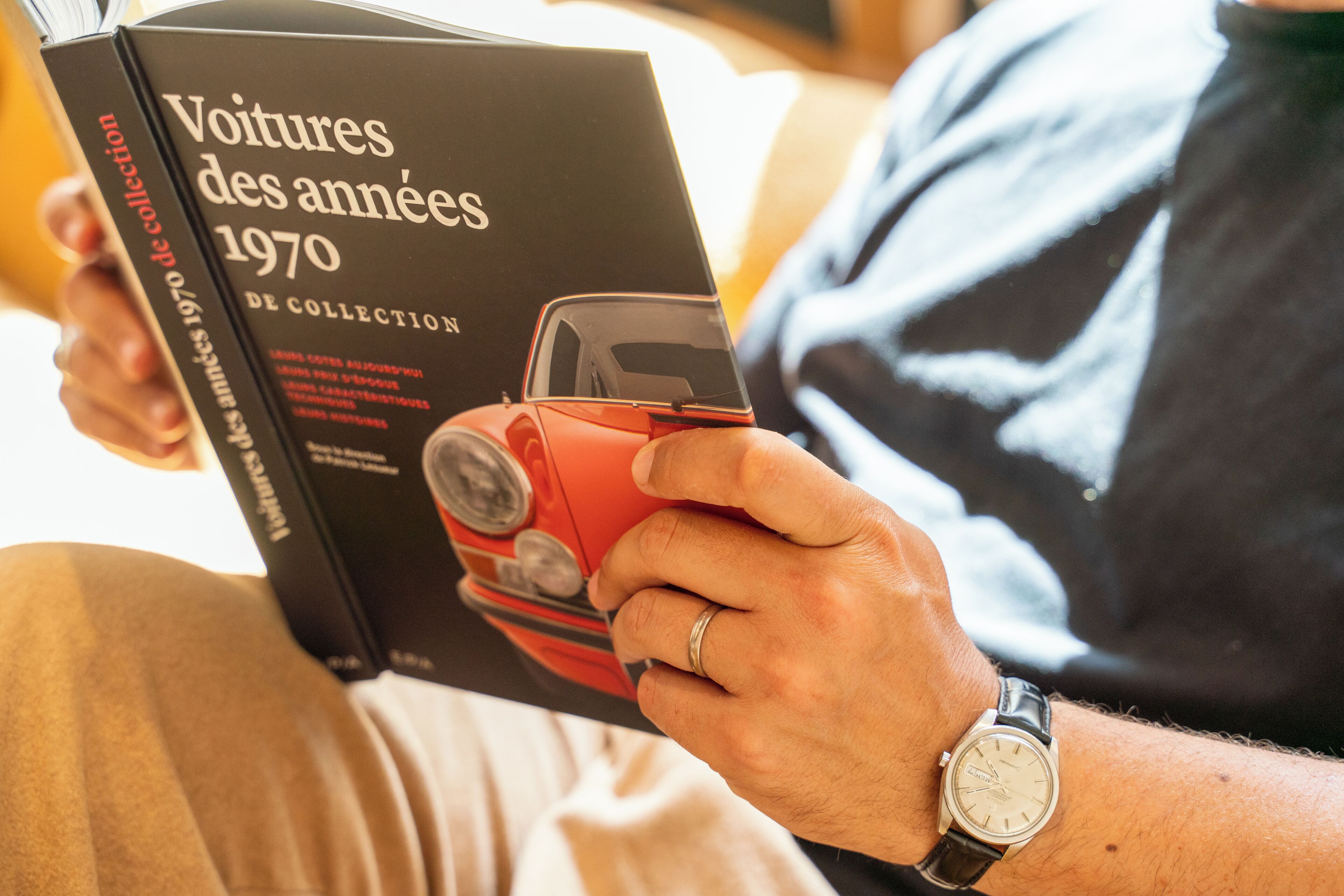 Een persoon houdt een boek vast met de titel 'Voitures des années 1970 de collection'.