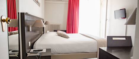 A hotel room with a bed, a desk, a mirror, and a television.
