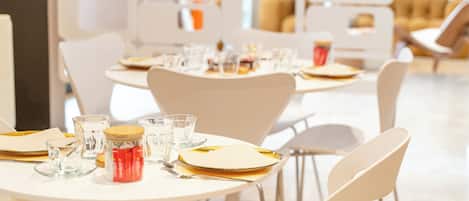 A modern dining area with round tables, white chairs, and neatly arranged glassware and cutlery.