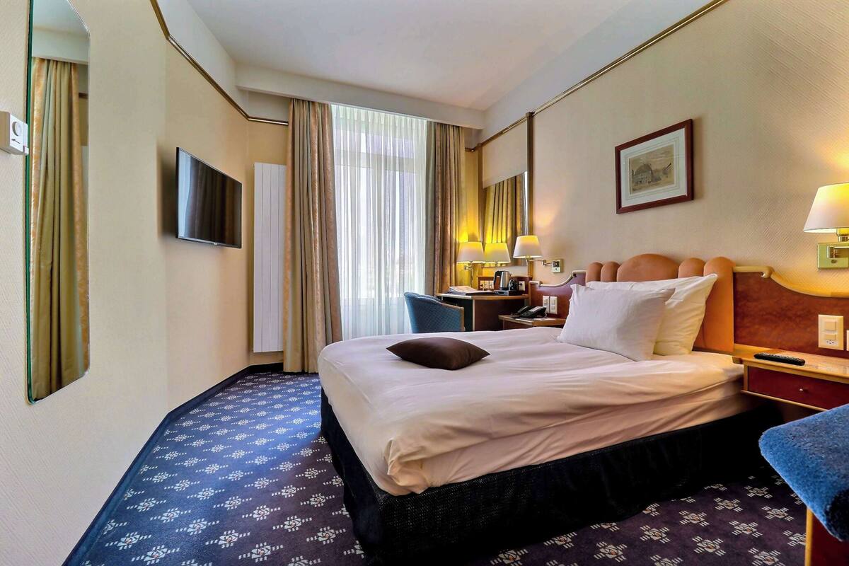Une chambre d’hôtel équipée d’un lit, d’un bureau, d’une chaise, d’une télévision et d’une fenêtre avec des rideaux.
