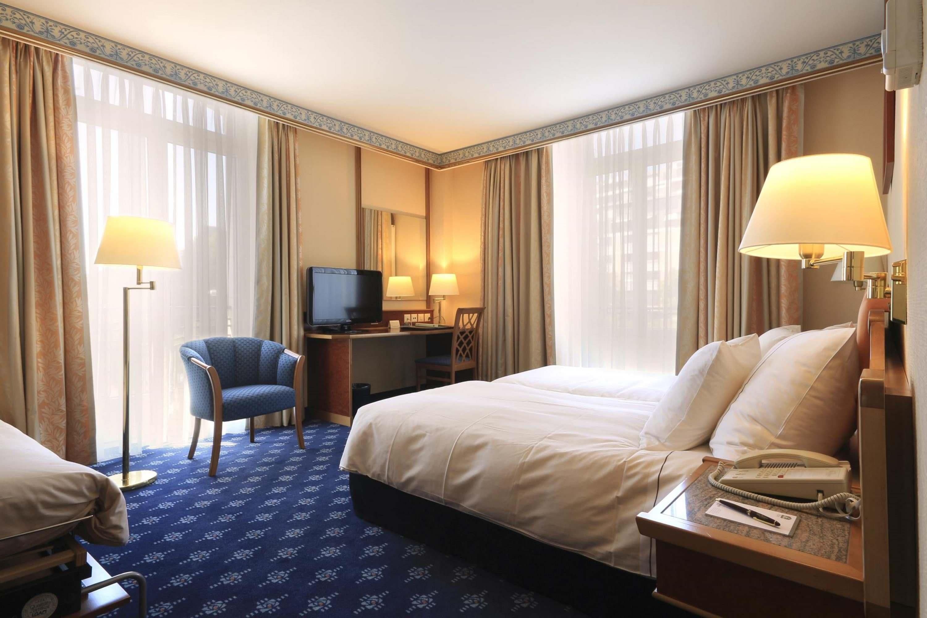Ein Hotelzimmer mit Bett, Schreibtisch, Stuhl, Fernseher und Lampen.
