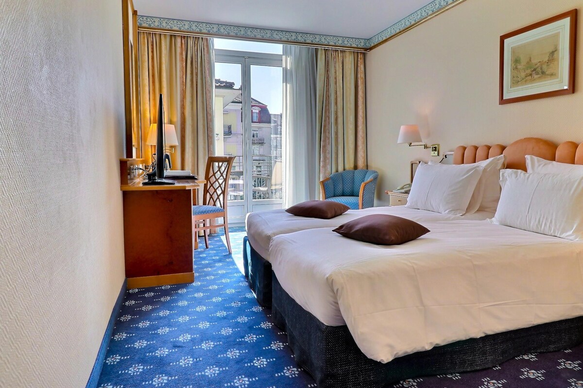 Habitación de hotel con cama, escritorio, silla y vistas al exterior.