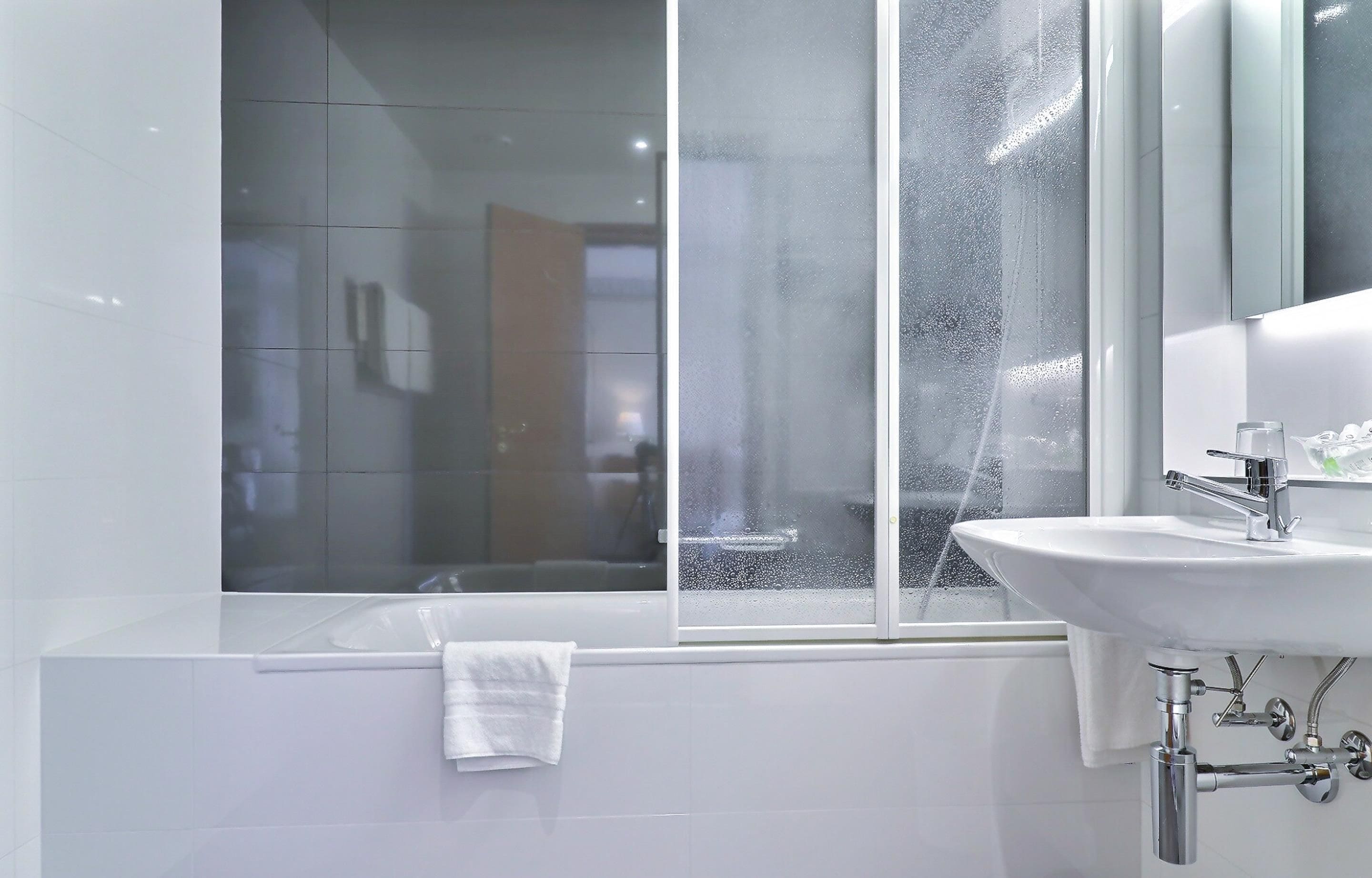 Ein modernes Badezimmer mit einer Badewanne, einem Waschbecken und einem Fenster mit Kondensation.