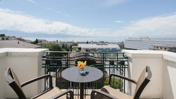 Un balcon avec une table ronde et des chaises, donnant sur un paysage urbain composé d’immeubles et d’une étendue d’eau.