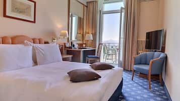 Ein Hotelzimmer mit einem großen Bett, einem Schreibtisch, einem Sessel, einem Fernseher und Blick ins Freie.