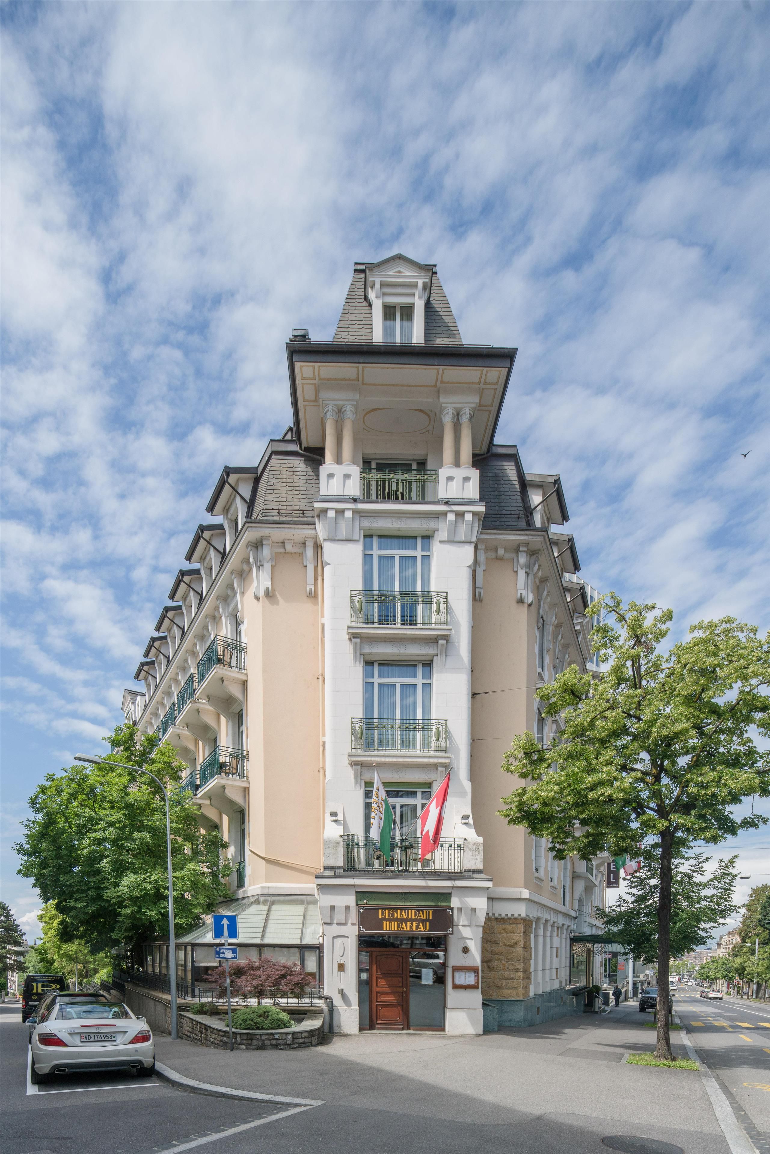 Un hôtel à plusieurs étages, de style architectural classique, qui se distingue par son entrée imposante, ses balcons et un drapeau.
