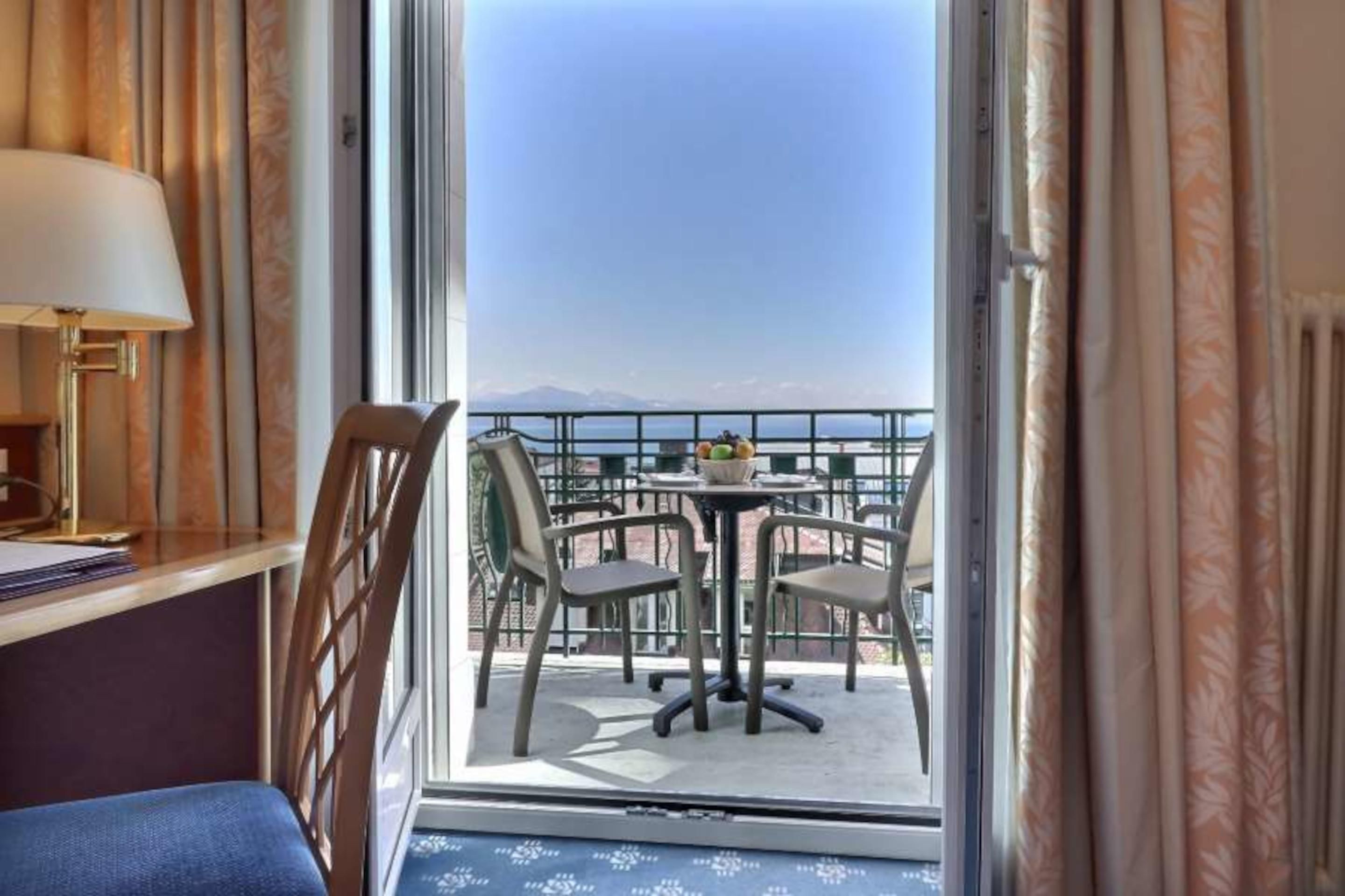 Quarto de hotel com varanda, uma mesa com cadeiras e vista para o mar.
