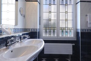 Un baño con dos lavabos, un espejo, una ventana con celosía decorativa y un radiador.