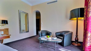 A hotel room with a bed, a desk with a lamp, a glass table with fruit, two chairs, a mirror, and a floor lamp. - Hotel Mirabeau, BW Signature Collection (Lausanne)