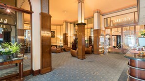 Un vestíbulo de hotel con una escalera monumental, una zona de estar y una recepción.