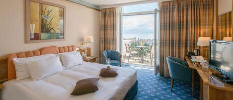 A hotel room with a large bed, a desk with a television, a chair, and a balcony with a view.
