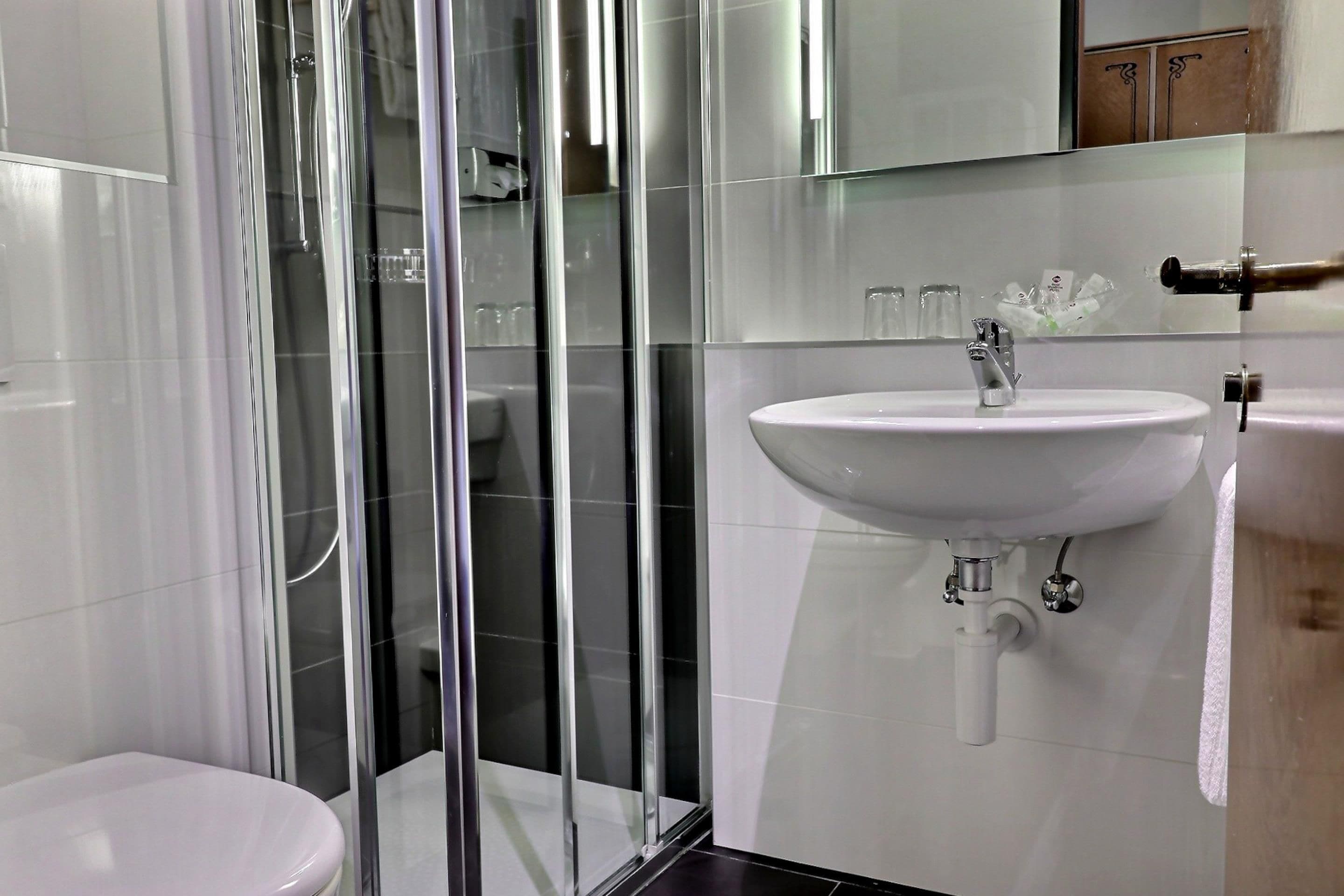 A modern bathroom with a glass shower enclosure, a white sink, and a mirror above it.