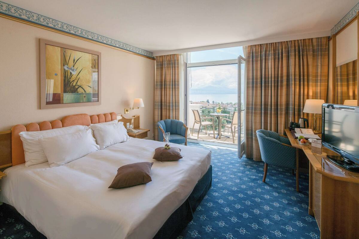 Une chambre d’hôtel avec un grand lit, un bureau avec une télévision, une chaise et un balcon avec vue.