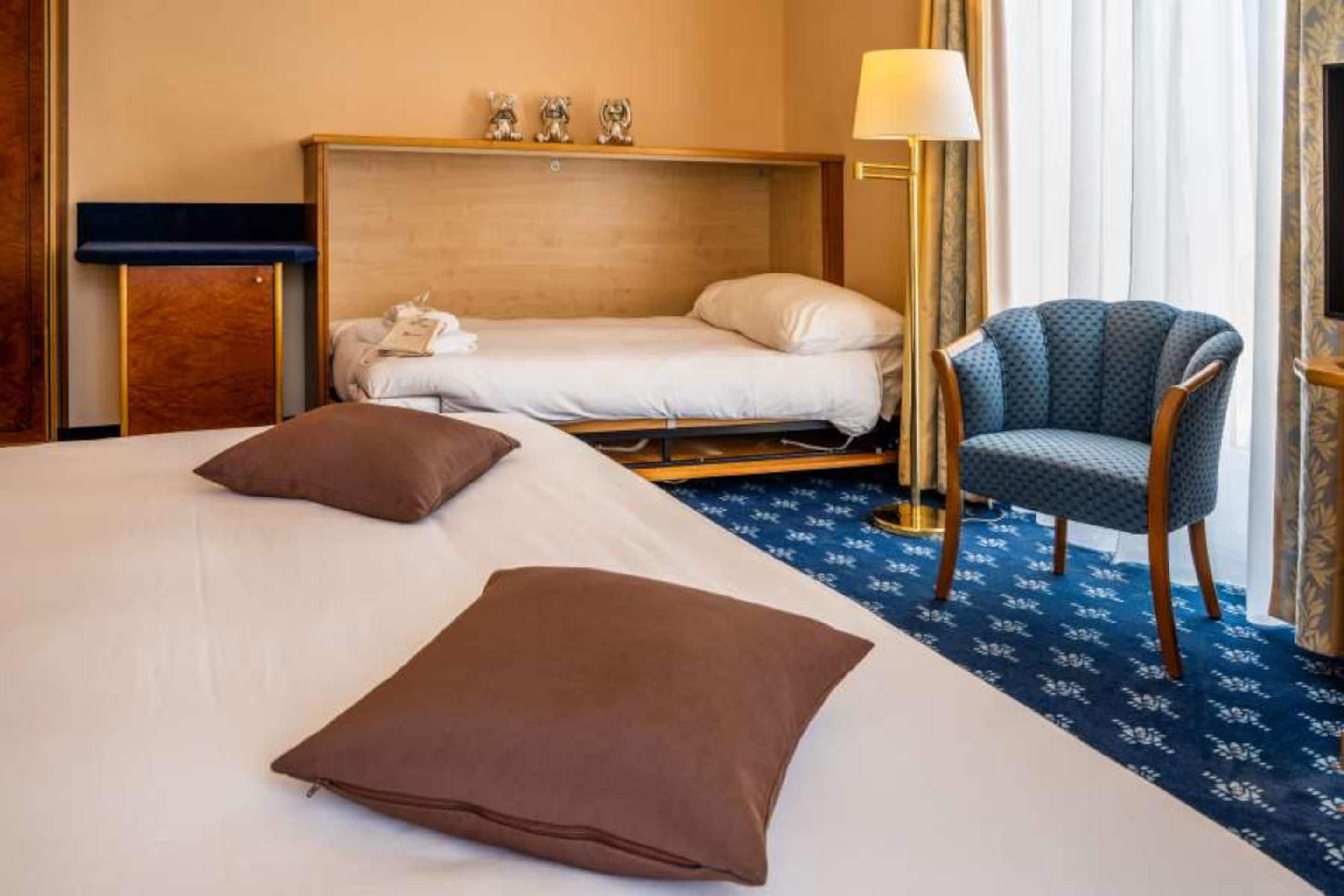 A hotel room with a bed, a chair, a desk, and a lamp.