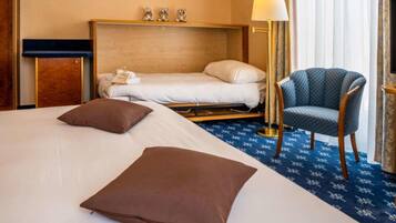 A hotel room with a bed, a chair, a desk, and a lamp.