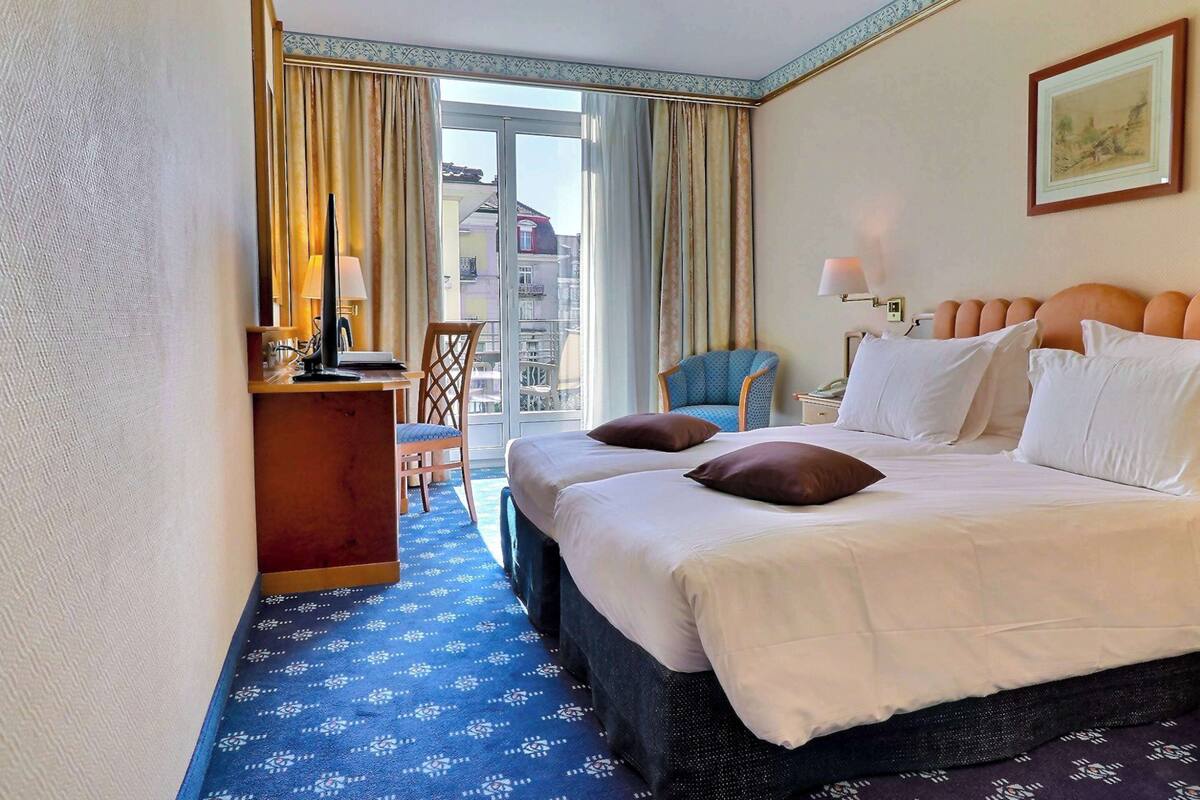 Une chambre d’hôtel avec un grand lit, un bureau, une chaise et un balcon avec des rideaux.