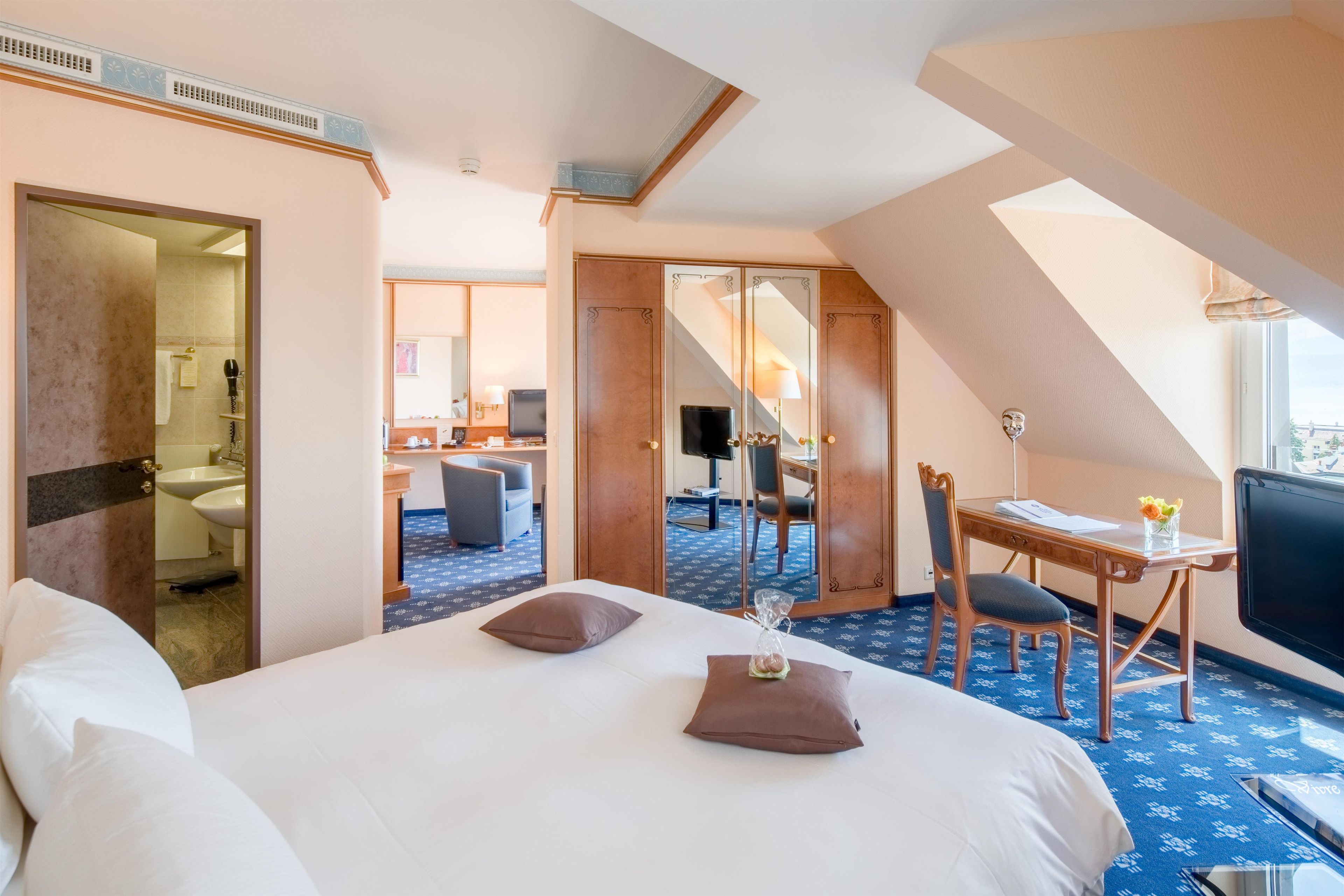 Habitación de hotel con una cama grande, un escritorio con silla, televisión y balcón con vista.