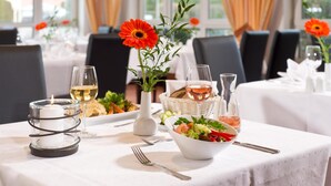 A dining table set with a candle, wine glasses, a bowl of salad, and a vase with flowers. - ACHAT Hotel Schwarzheide Lausitz (Schwarzheide)