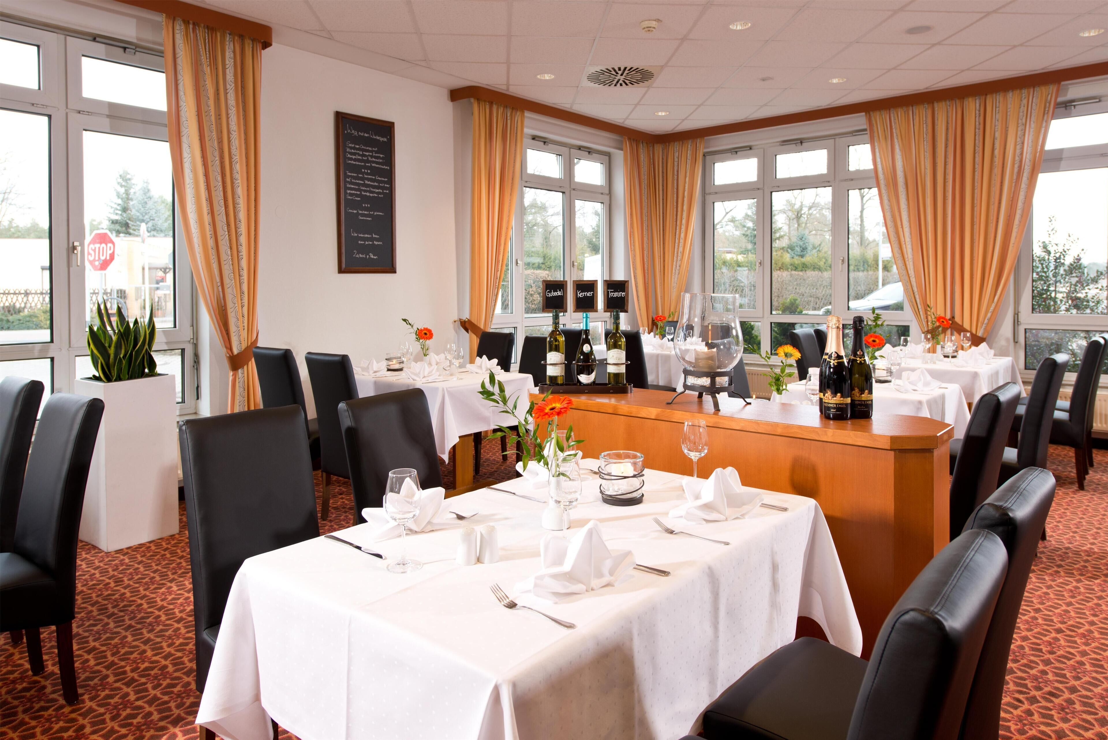 Een eetgedeelte met gedekte tafels, een menukaart, wijnflessen en uitzicht op het buitengebied.