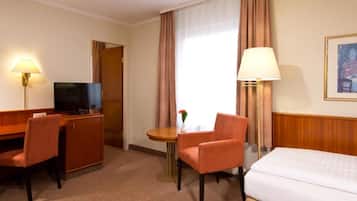 A hotel room with a bed, a desk with a chair, a television, a lamp, and a window with curtains.