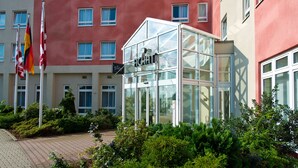 A modern hotel with a glass conservatory, multiple flags, and a red building facade. - ACHAT Hotel Schwarzheide Lausitz (Schwarzheide)