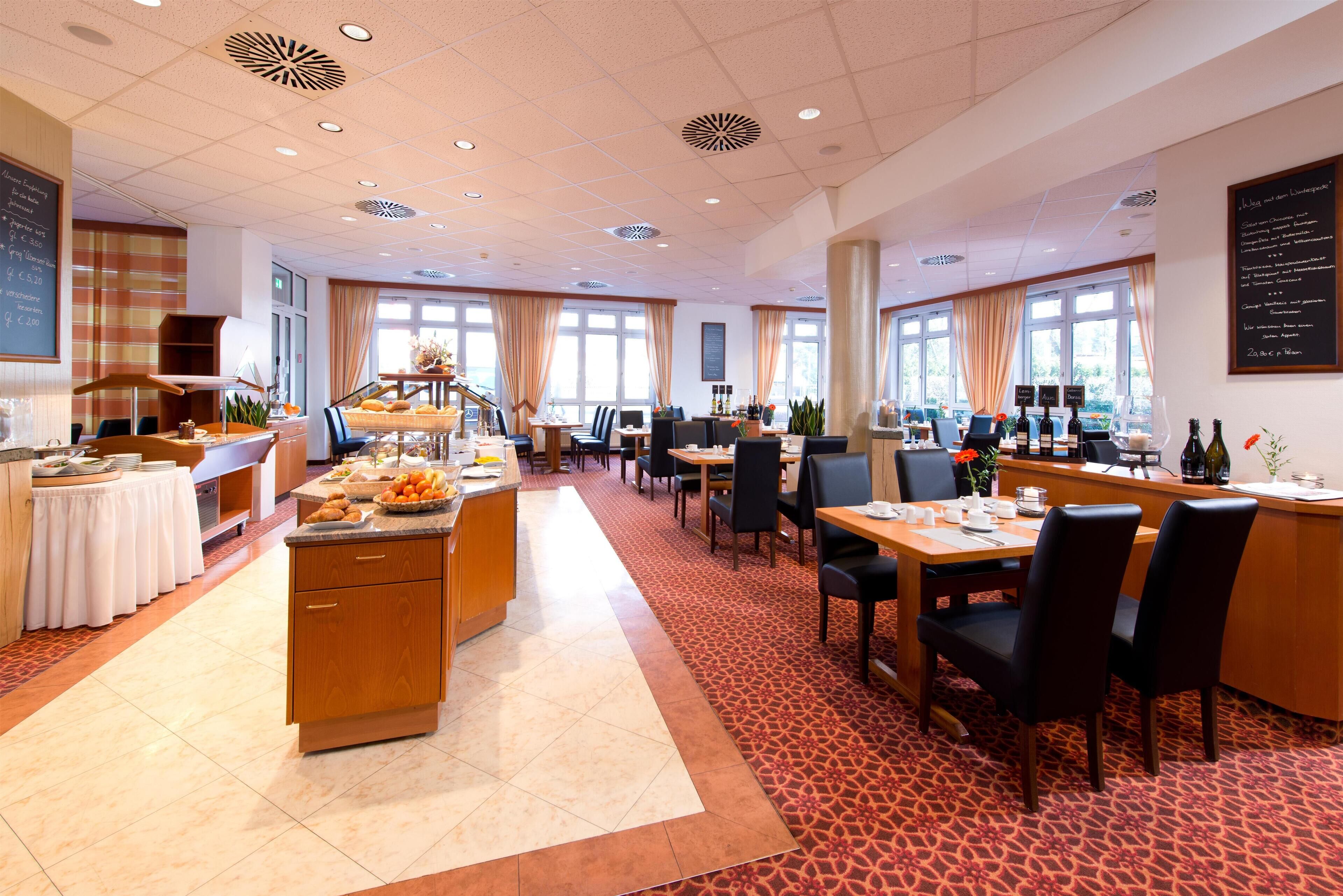 Un vaste espace de restauration dans l’hôtel, avec de nombreuses tables et chaises, un buffet et de grandes fenêtres laissant entrer la lumière naturelle.