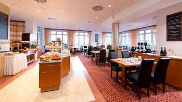 Un vaste espace de restauration dans l’hôtel, avec de nombreuses tables et chaises, un buffet et de grandes fenêtres laissant entrer la lumière naturelle.