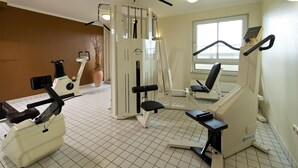 A fitness center with various exercise machines, a large window, and a potted plant. - ACHAT Hotel Schwarzheide Lausitz (Schwarzheide)