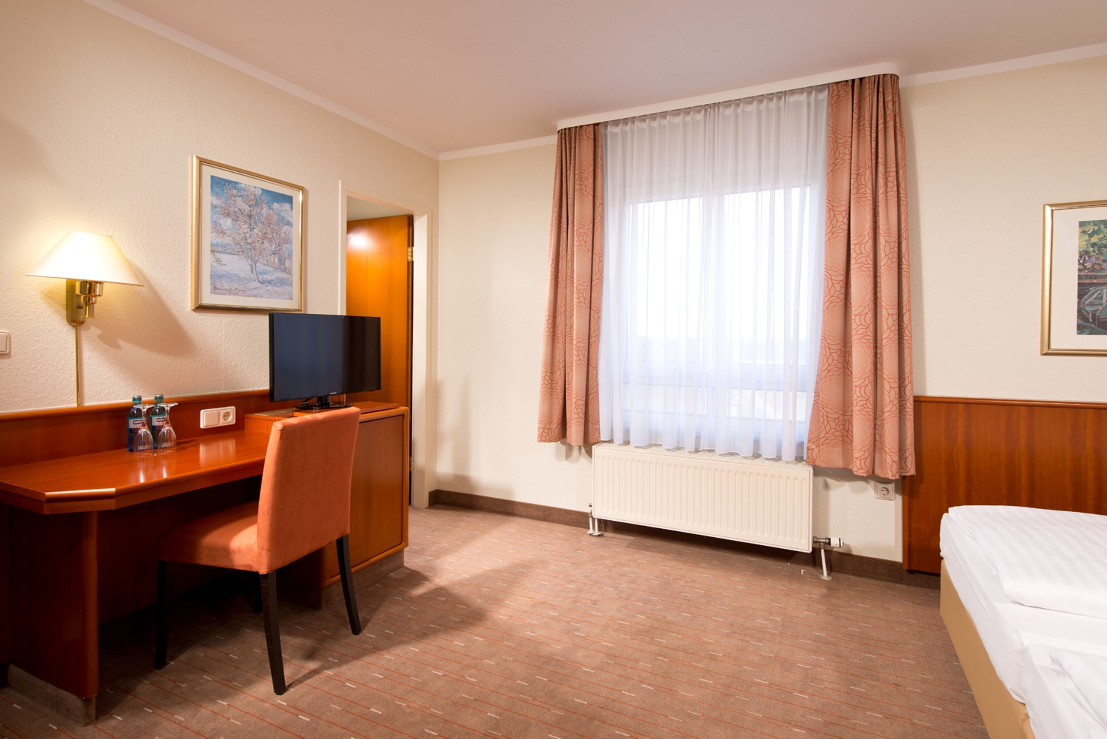 A hotel room with a wooden desk, chair, bed, and a window with curtains.
