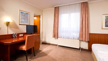 Una habitación de hotel con escritorio de madera, silla, cama y ventana con cortinas.