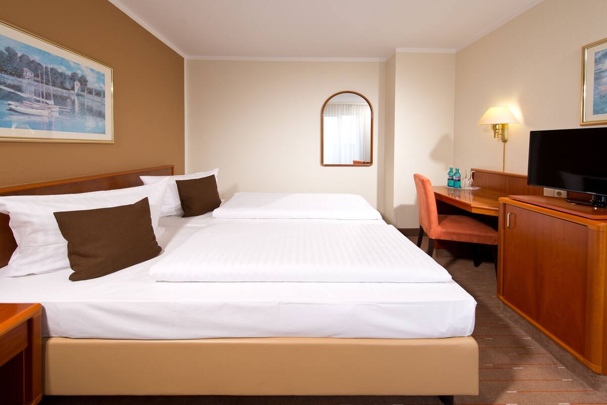 Une chambre d’hôtel avec deux lits, un bureau, une télévision et un miroir.