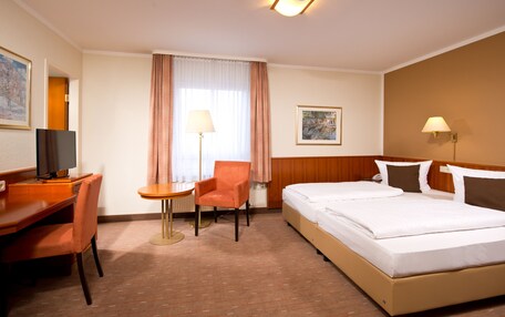 A hotel room with a bed, a desk with a chair, a lamp, and a painting on the wall.