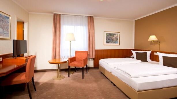 A hotel room with a bed, a desk with a chair, a lamp, and a painting on the wall. - ACHAT Hotel Schwarzheide Lausitz (Schwarzheide)