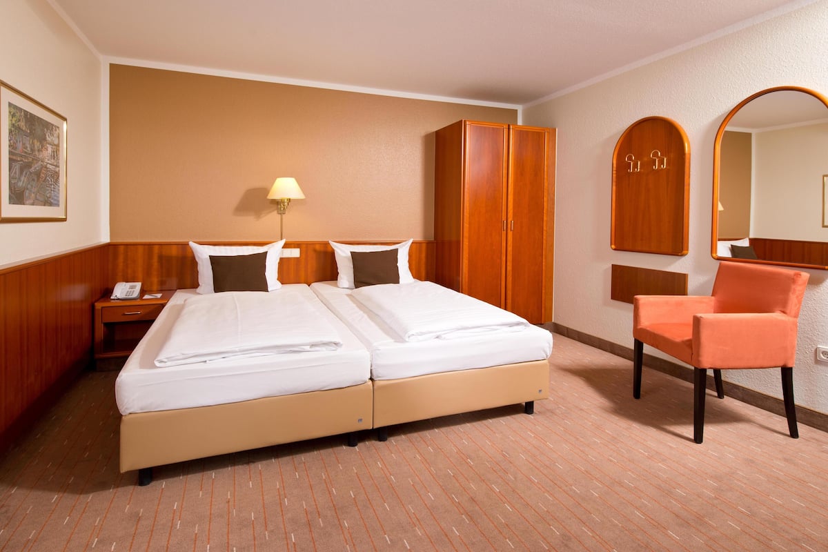 Une chambre d’hôtel avec un lit double, une armoire en bois, une chaise, une table de chevet, une lampe et un miroir.