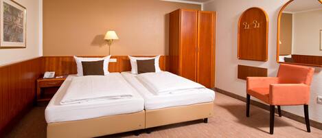Una habitación de hotel con cama doble, un armario de madera, una silla, una mesita de noche, una lámpara y un espejo.