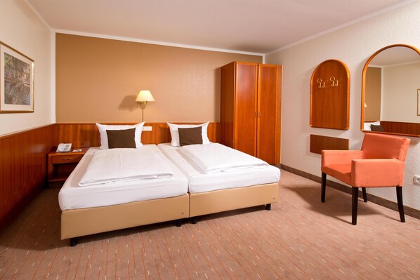 A hotel room with a double bed, a wooden wardrobe, a chair, a nightstand, a lamp, and a mirror. - ACHAT Hotel Schwarzheide Lausitz (Schwarzheide)
