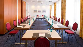 Une salle de conférence avec de longues tables, des chaises rouges et des bouteilles d’eau bleues.