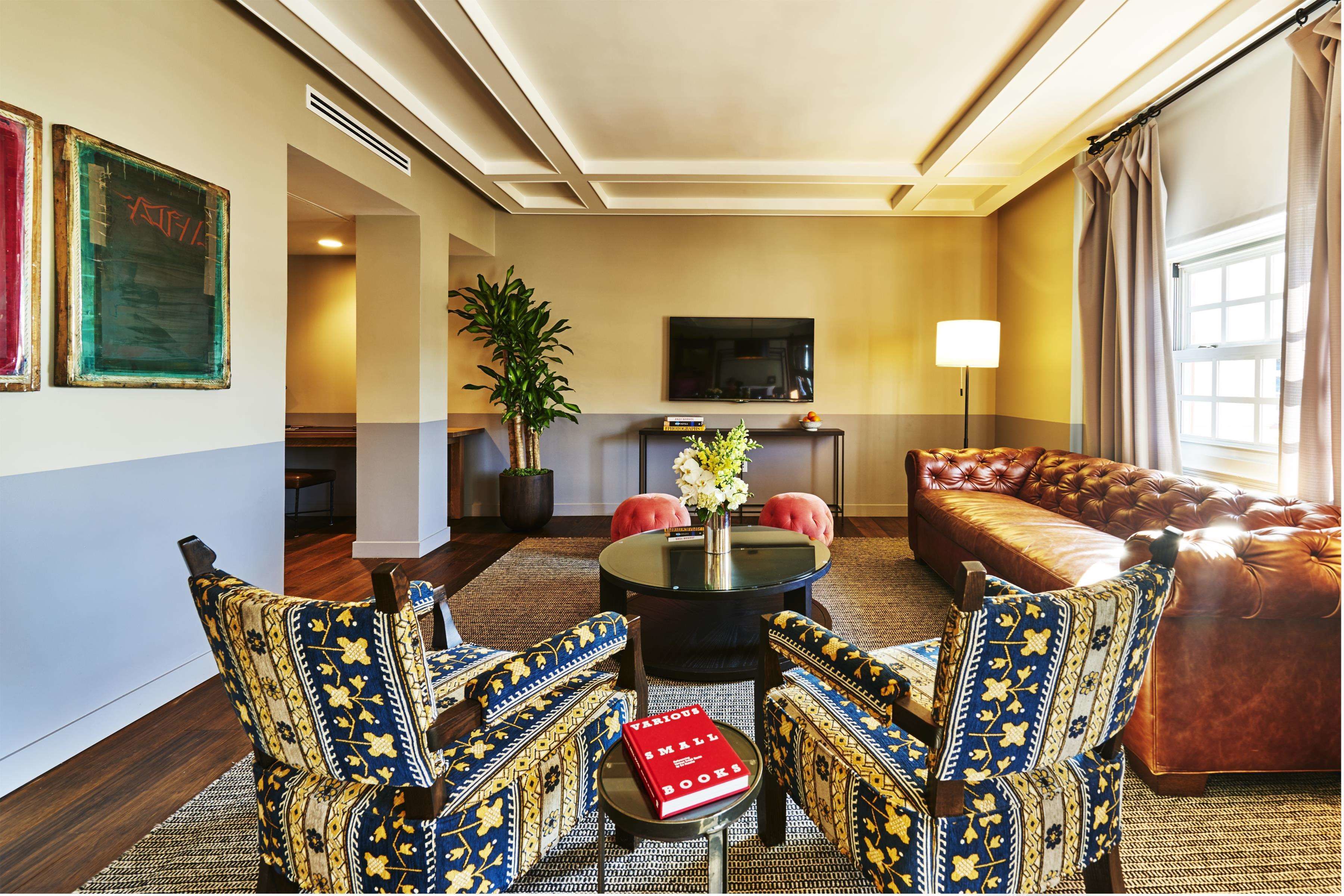 A living room with a brown leather sofa, patterned armchairs, a round coffee table, and a flat-screen TV on a stand.